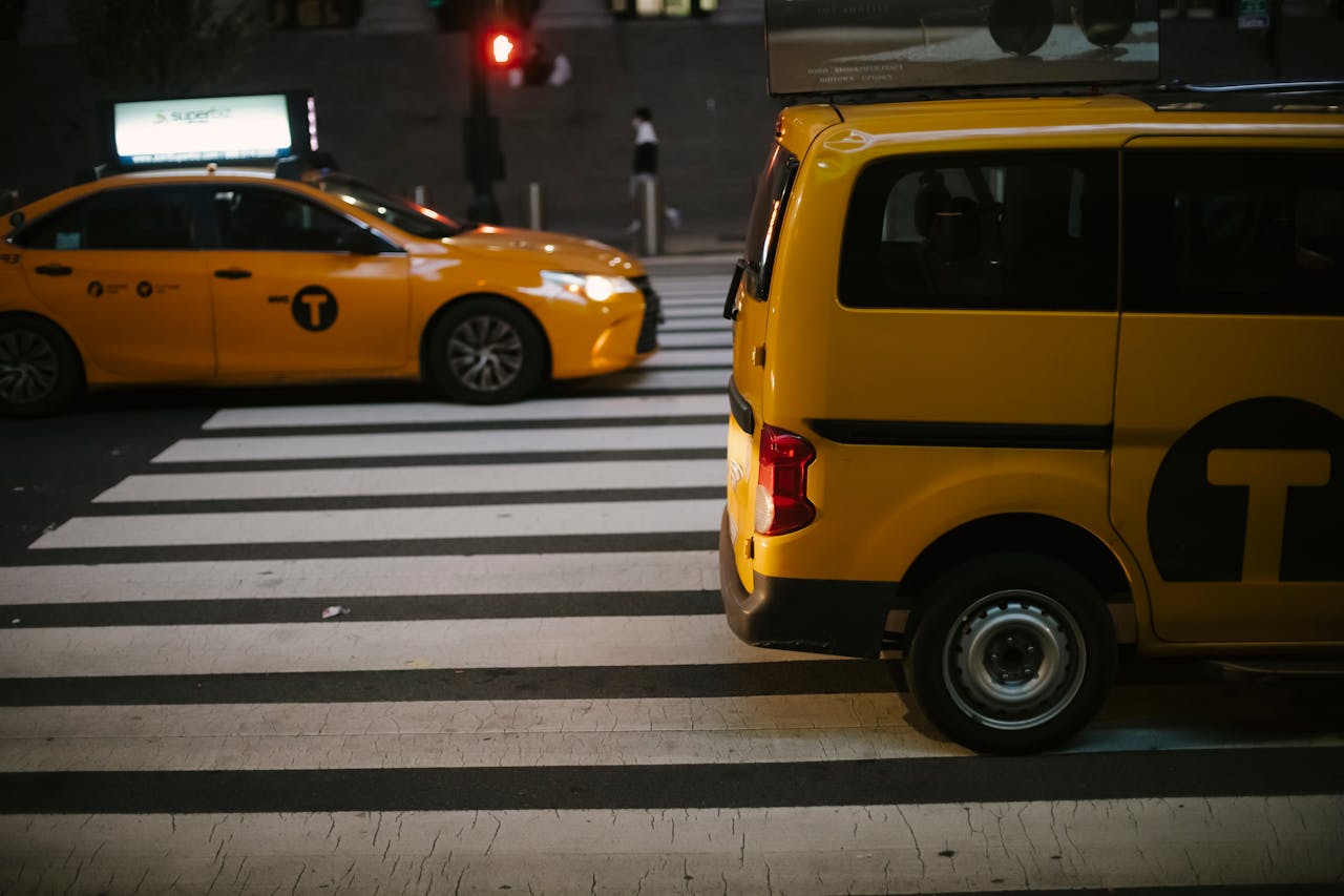 Yellow taxis on a urban street at night, captured at a bustling crosswalk under city lights.