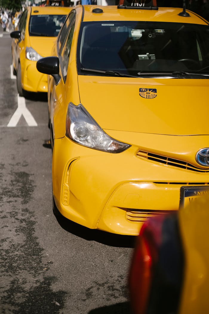 Close-up view of yellow taxis parked in a row on a sunny city street.